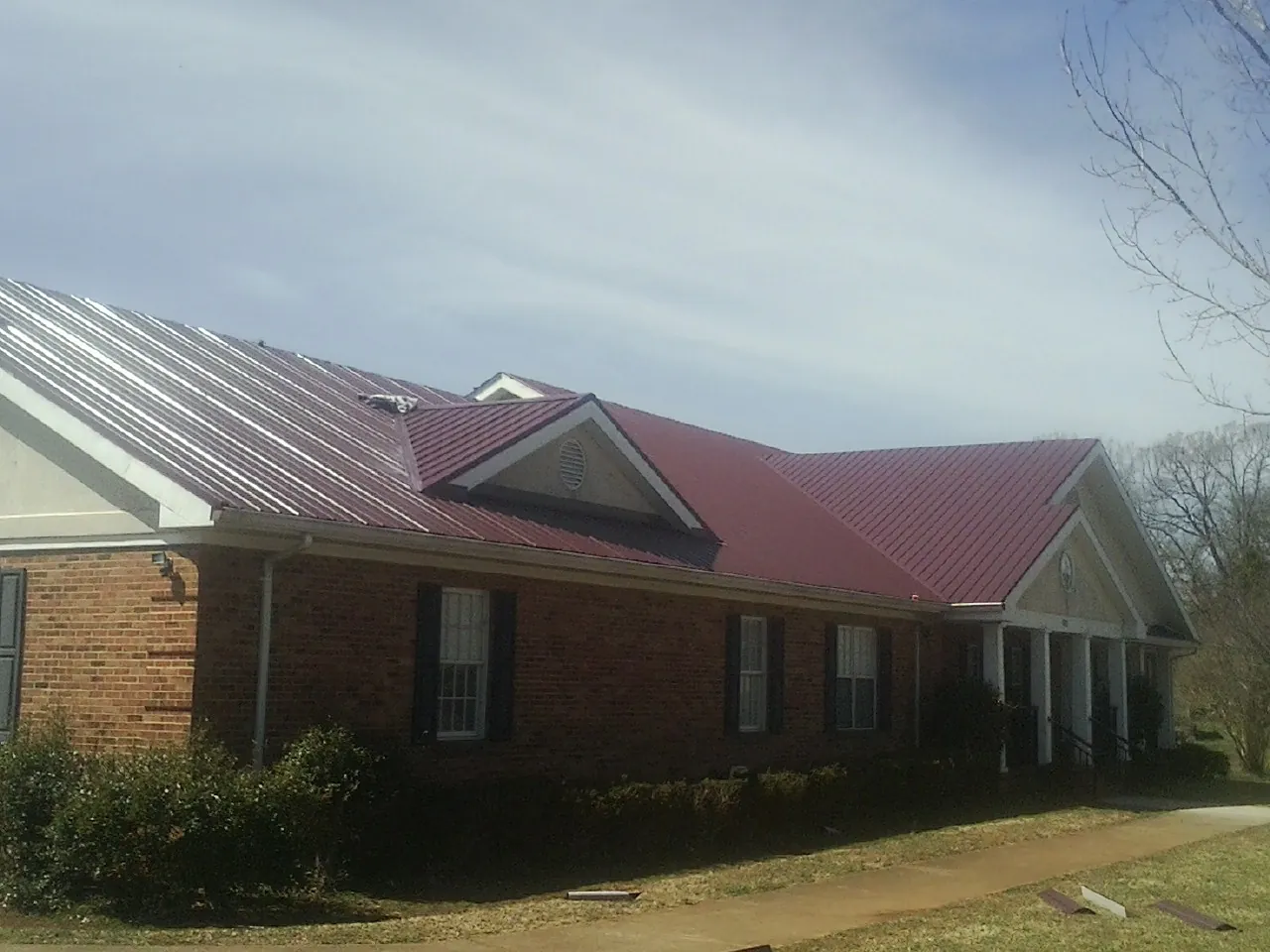Red metal roof with gabled entries on a long brick building, from a Hail Damage Roof Repair job in Hull