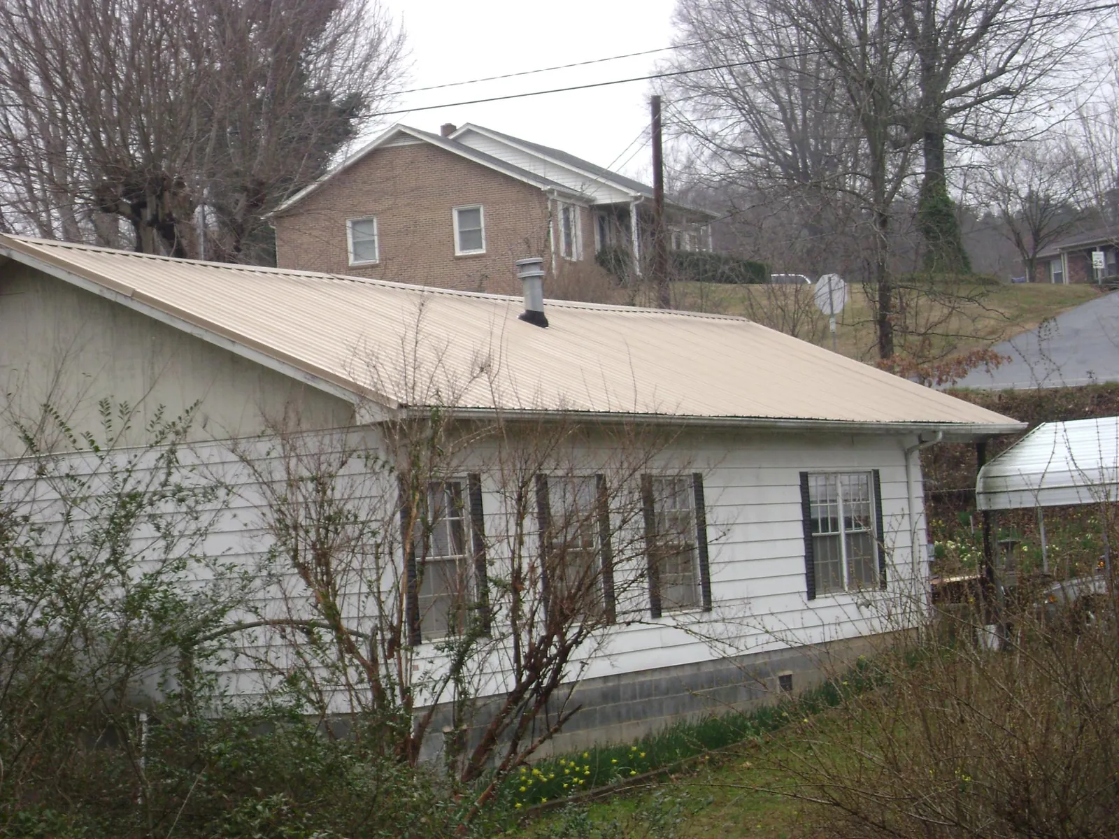 Tan metal roof on a white sided house set into a hillside — Commercial Roofing by Roofing Brothers in Hull